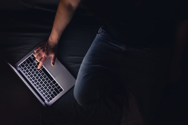Busy man networking on laptop late at night, typing text, working overtime.